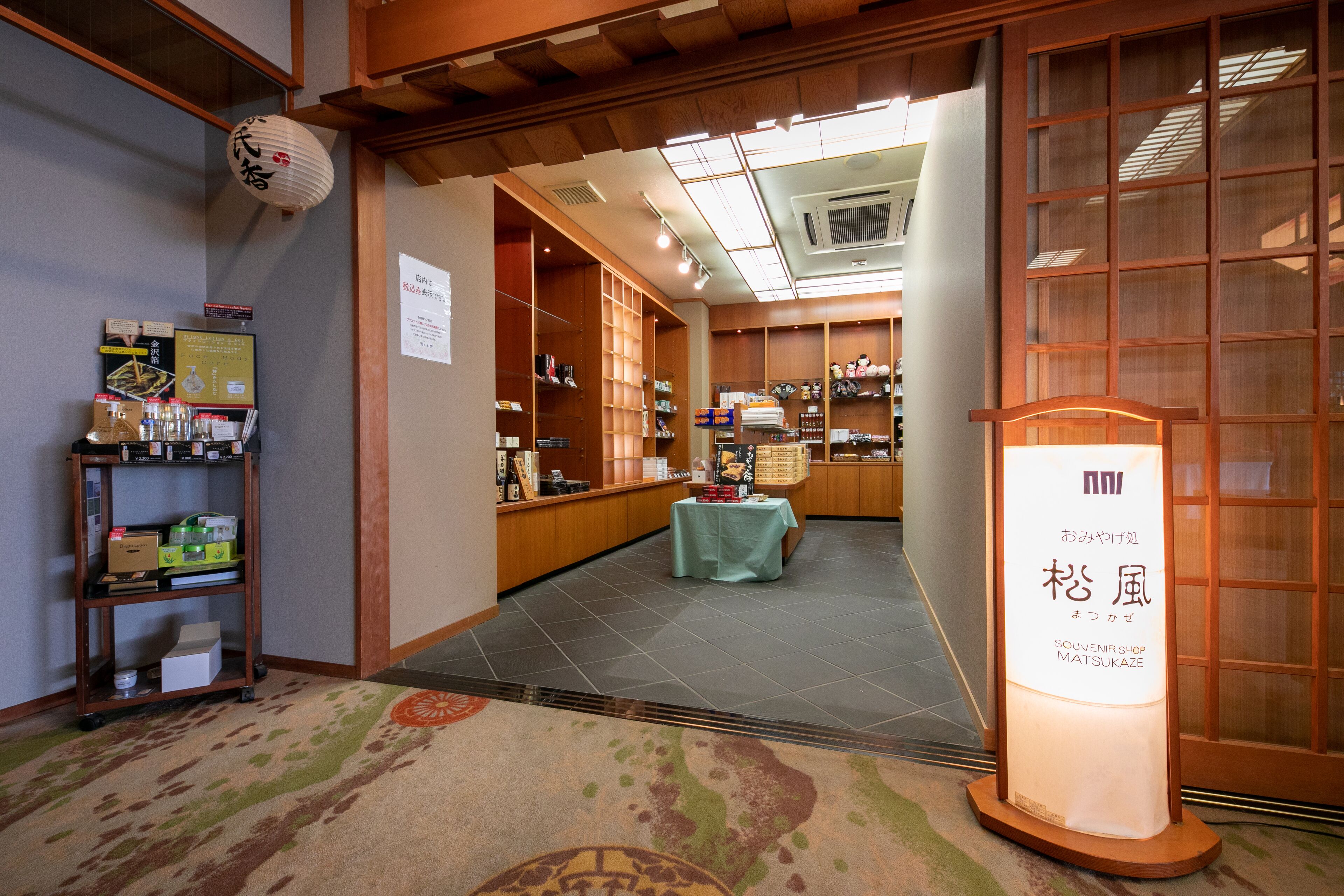 A traditional Japanese interior with a reception desk, shelves with merchandise, and a sign for a souvenir shop.