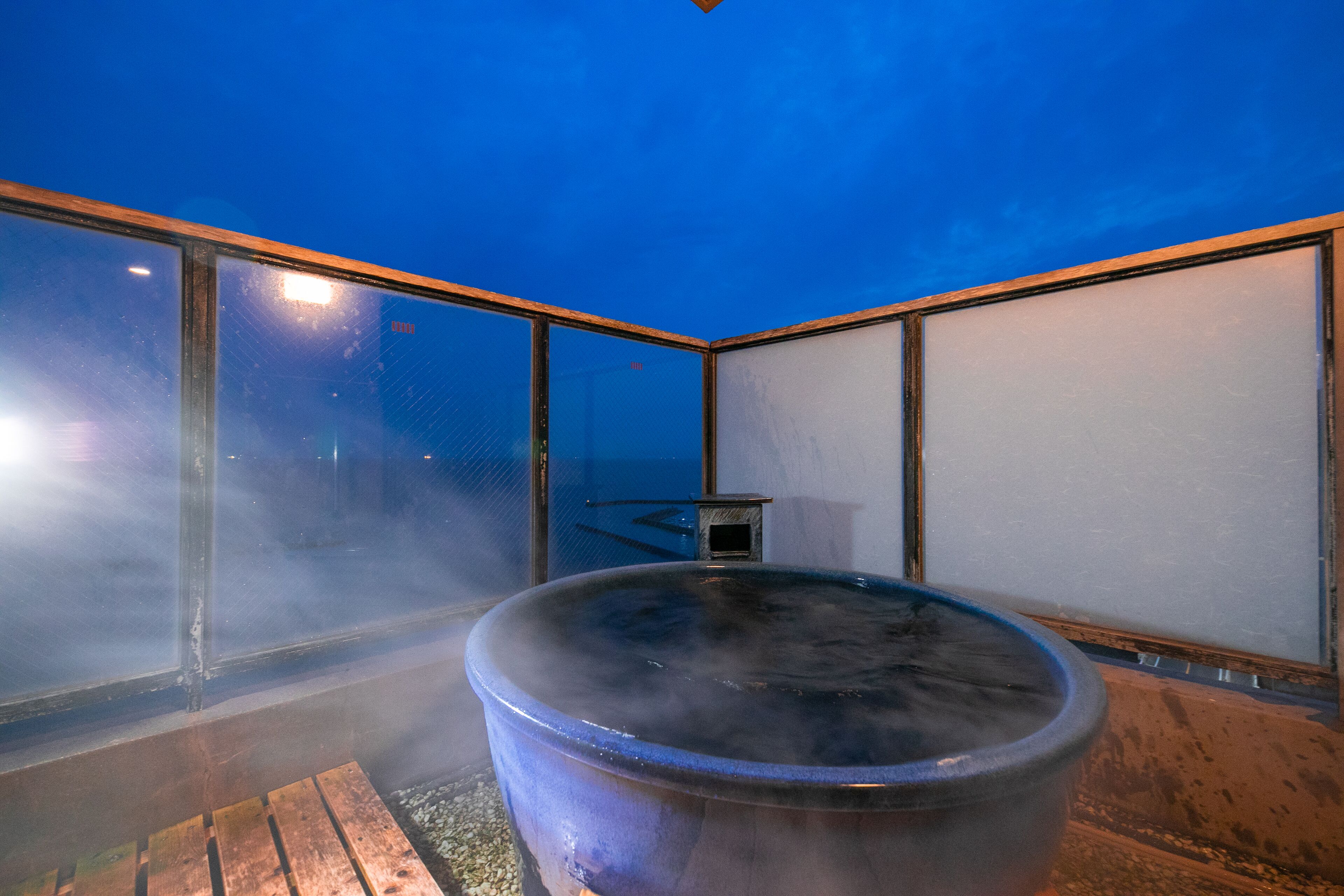 A hot tub in a room with large windows and a wooden floor.
