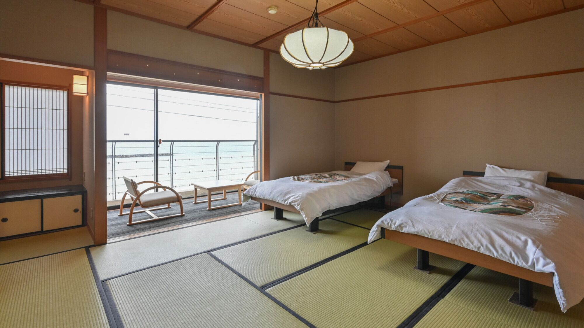 A traditional Japanese room with tatami flooring, two beds, a sliding door to a balcony, and a hanging light fixture.