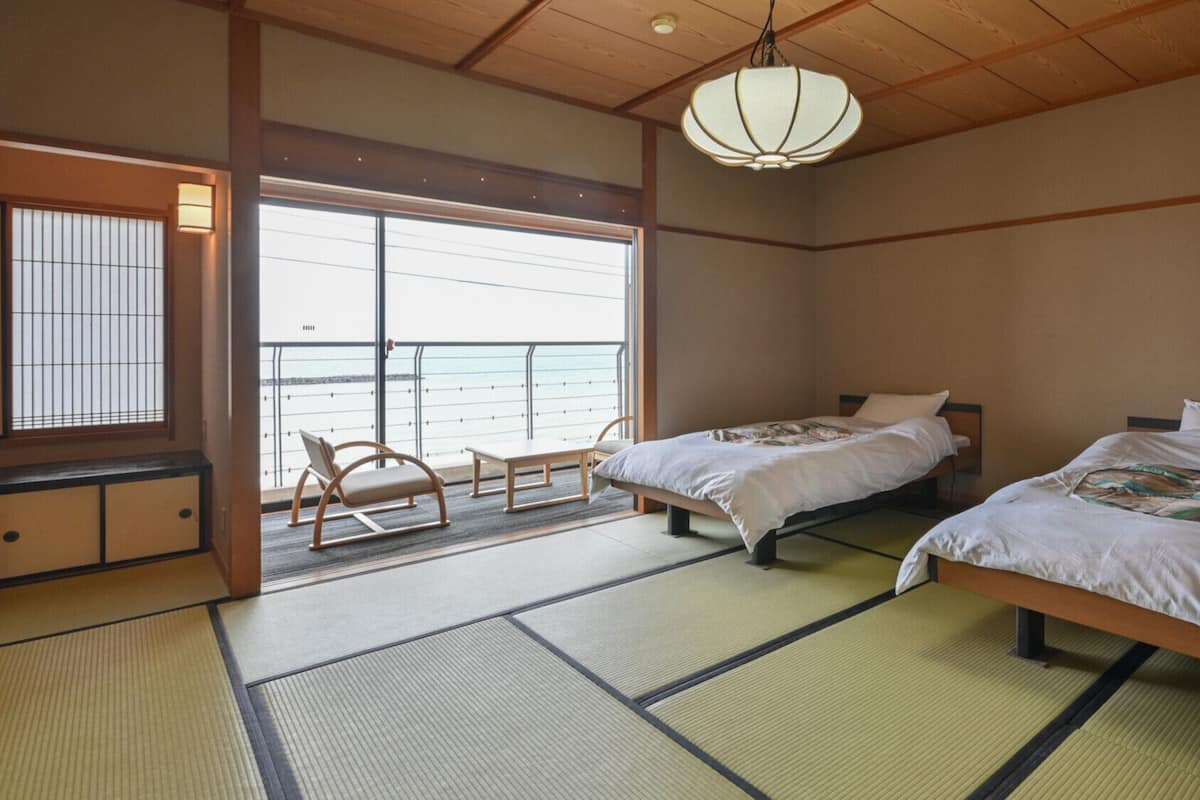 A traditional Japanese room with tatami flooring, two beds, a sliding door to a balcony, and a hanging light fixture.