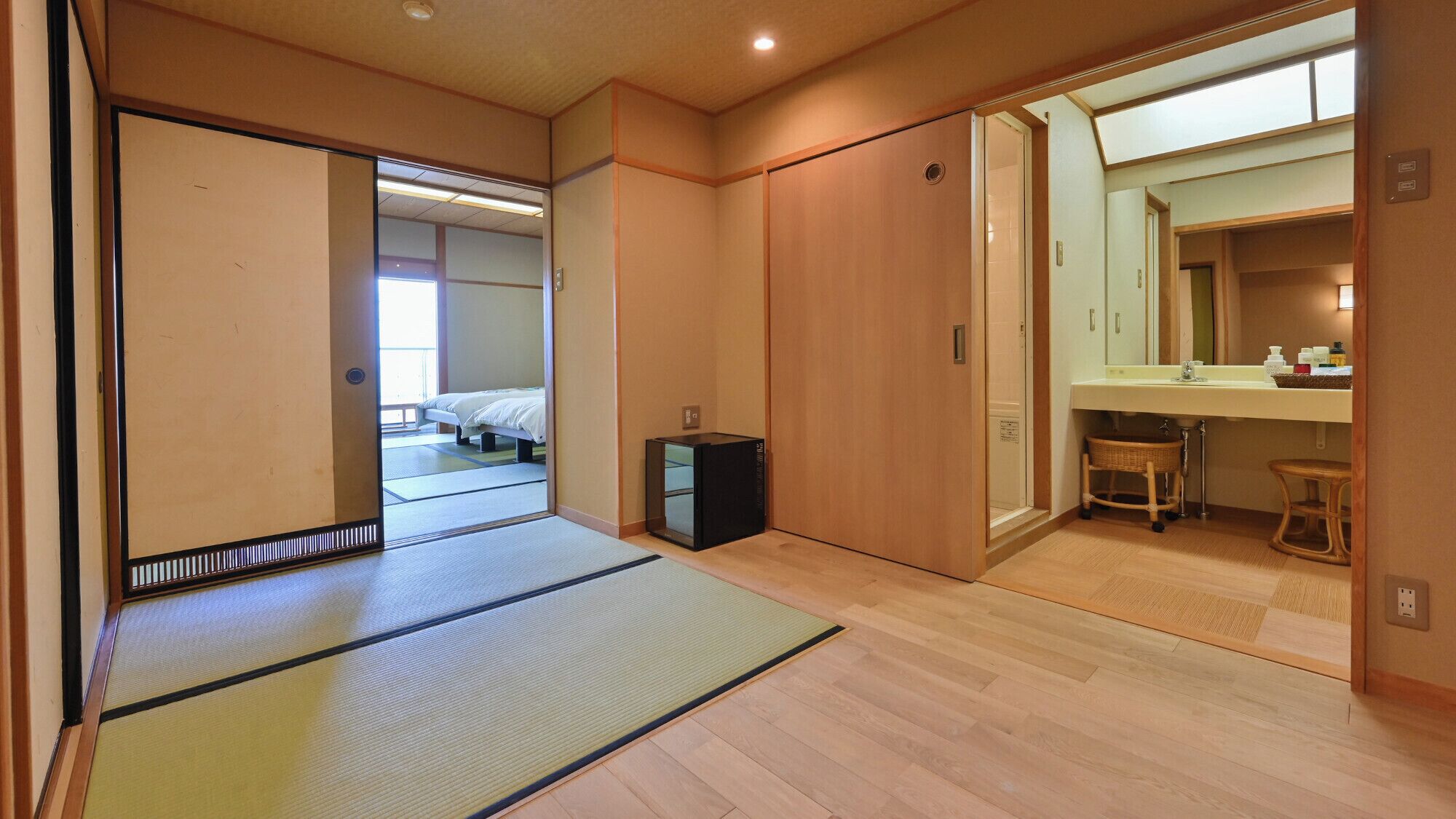 A traditional Japanese room with tatami flooring, a bed, a small cabinet, and a bathroom with a sink and mirror.