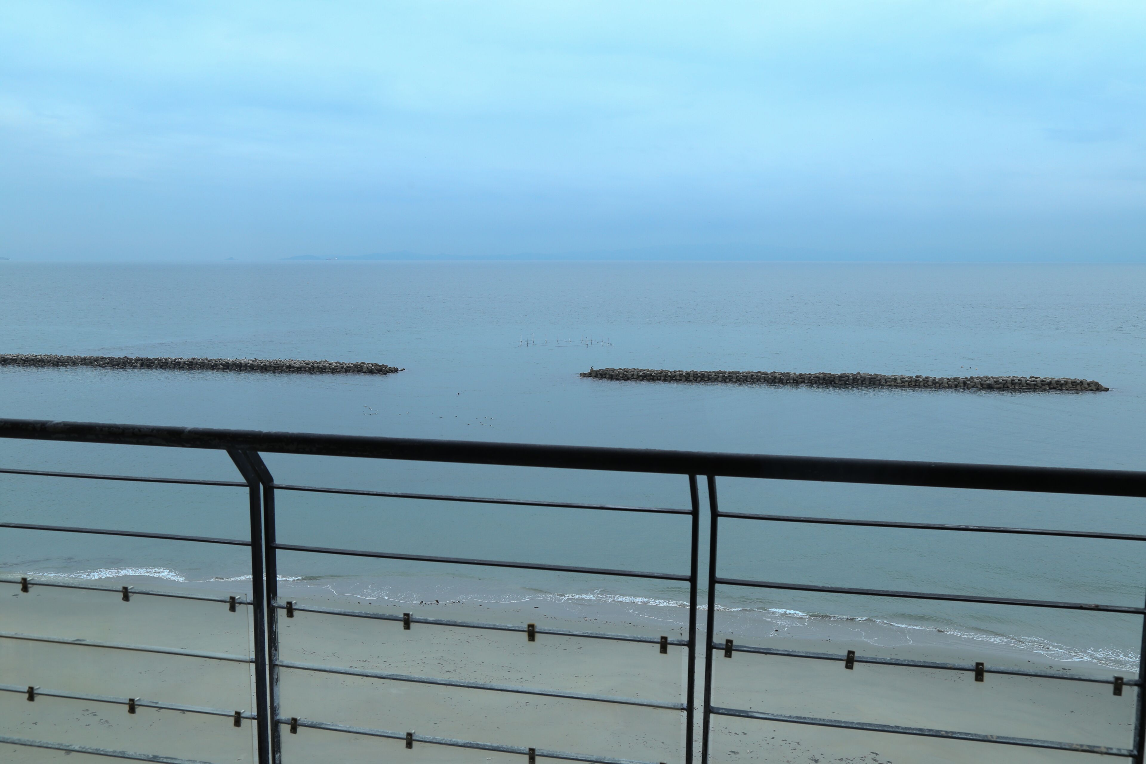 Vista de una playa con una baranda metálica al frente.