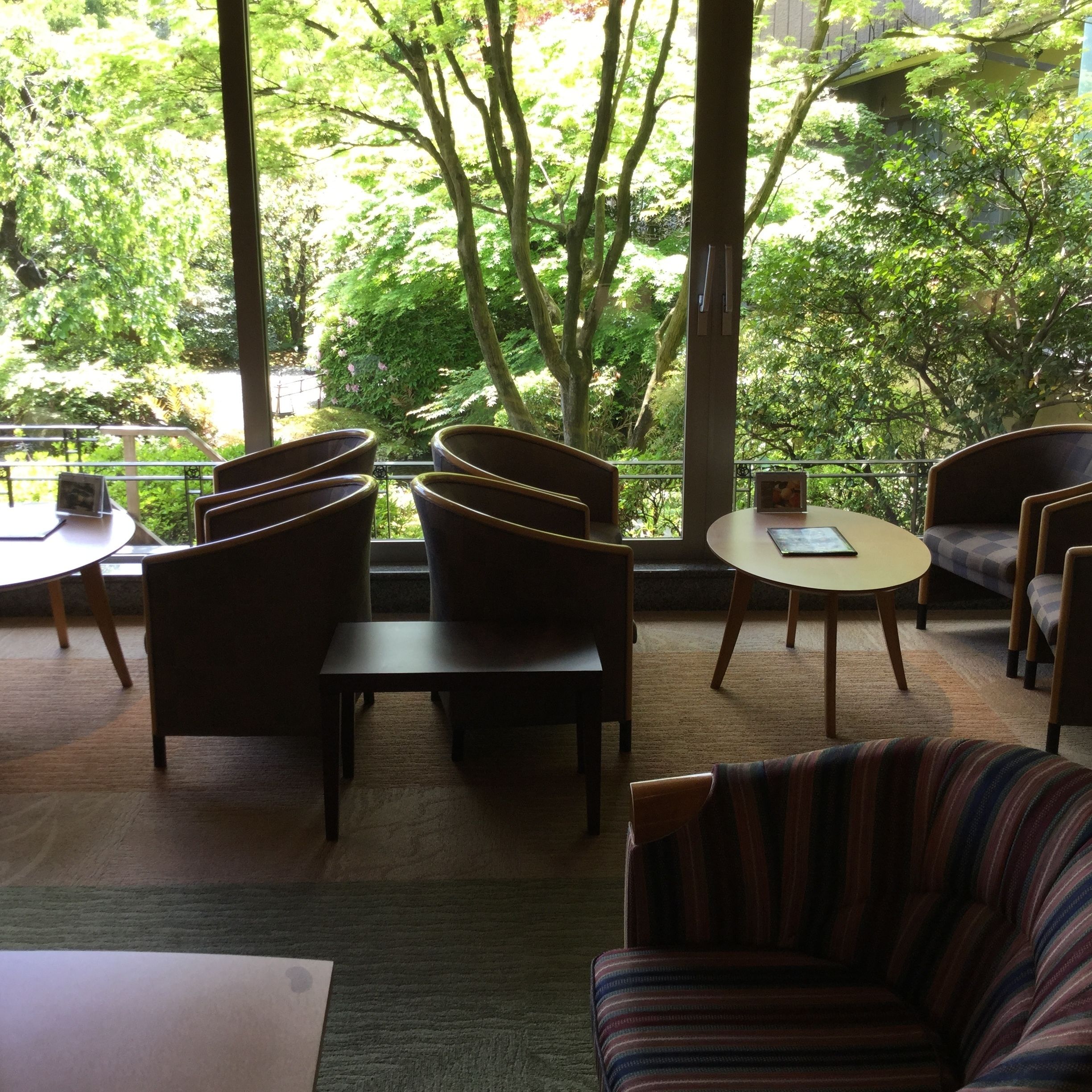 Una habitación con vistas a árboles a través de amplios ventanales, una mesa redonda y varias sillas.