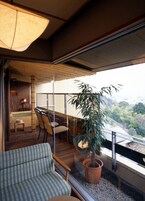 A balcony with a view of a cityscape, a potted plant, and a seating area with a chair and a sofa.