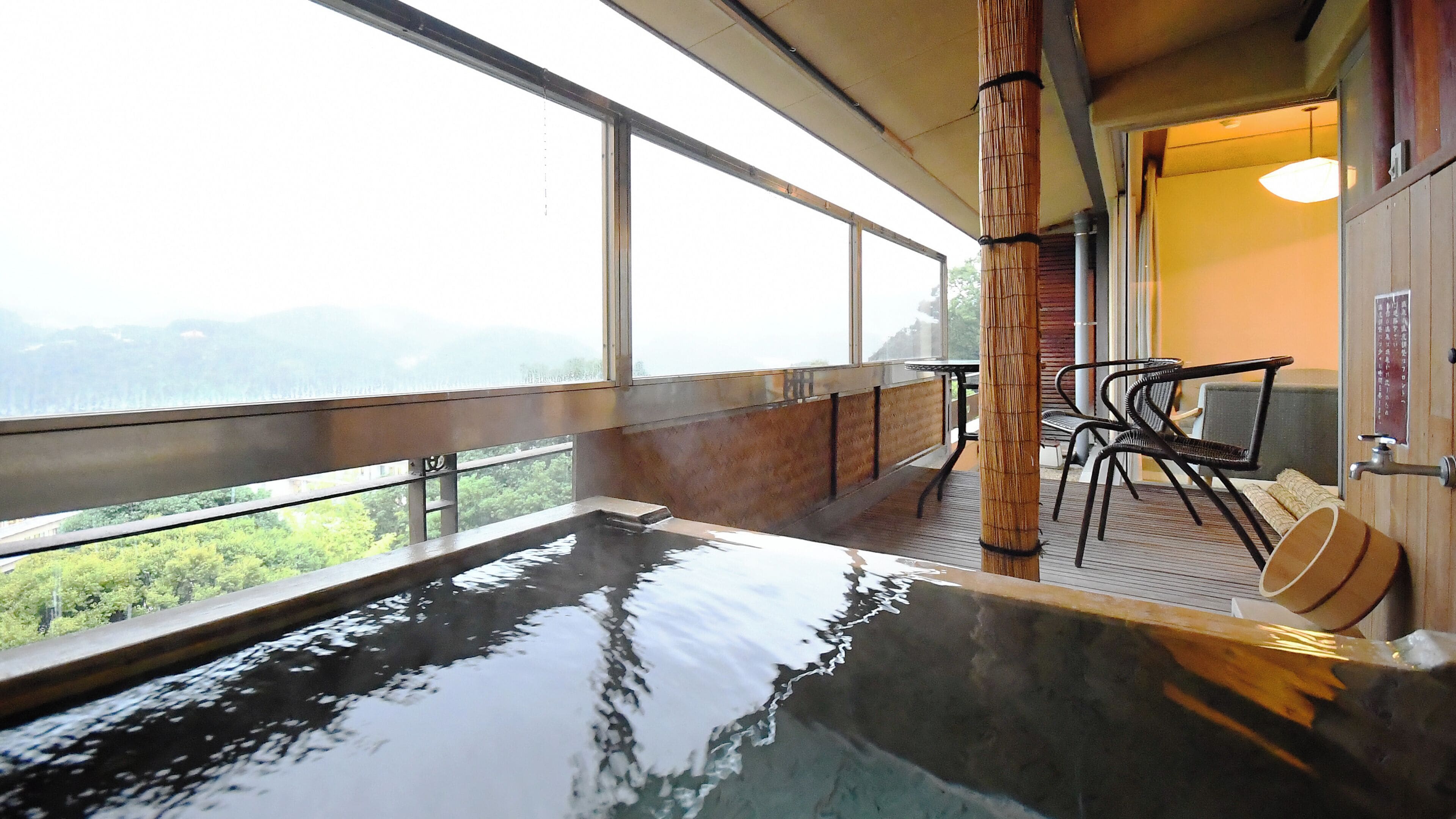 Ein Thermalbadbereich mit Blick auf die Berge, einer Bambussäule und einem Tisch mit Stühlen.