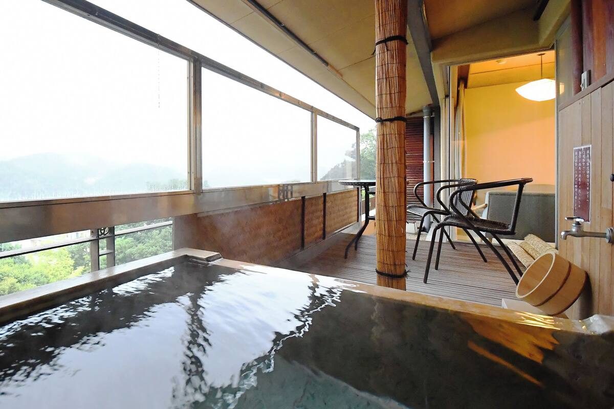 A hot spring bath area with a view of the mountains, a bamboo pillar, and a table with chairs.