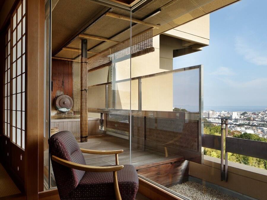 A balcony with a view of the city, a wooden chair, and a glass partition.