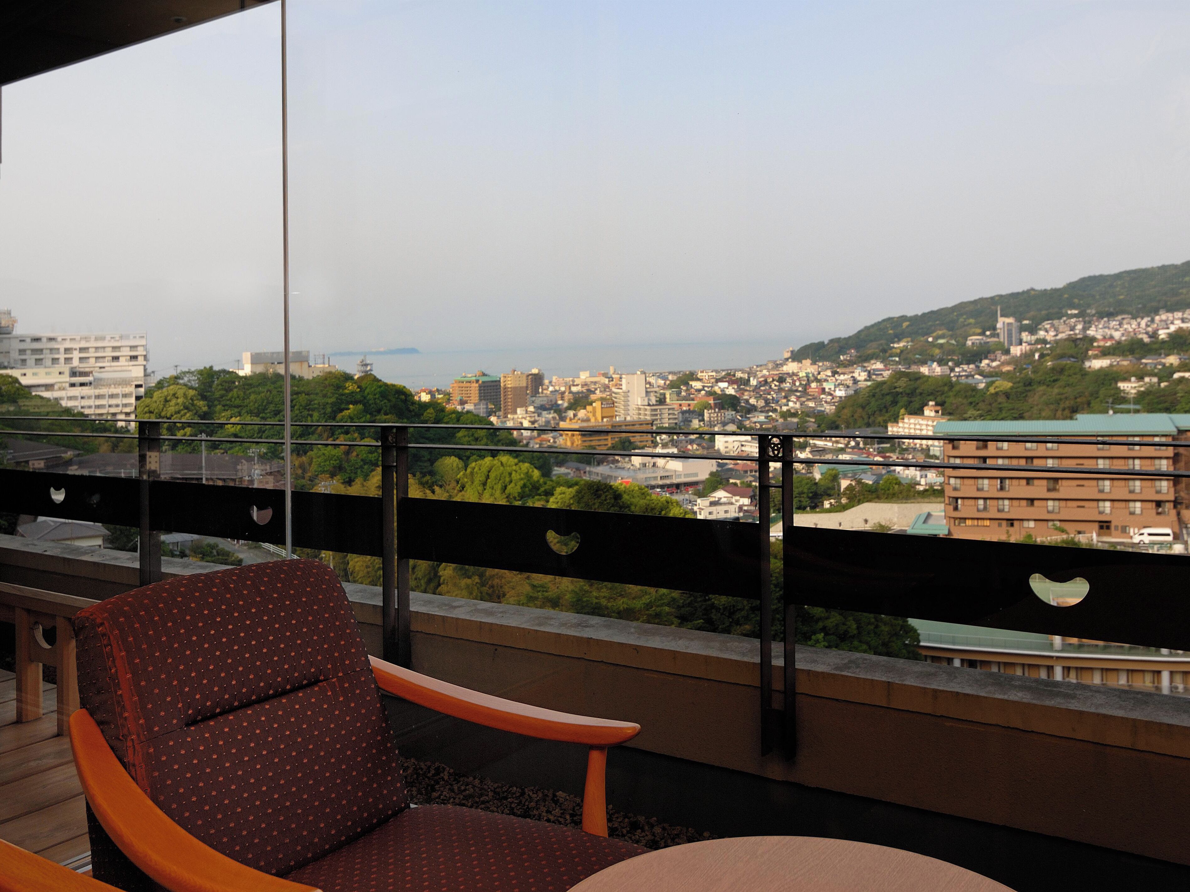 A balcony with a view of a cityscape, a chair, and a table.