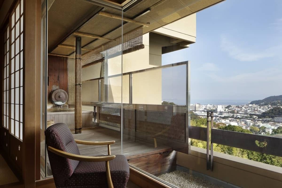 Una habitación con vistas a un paisaje urbano, una puerta corrediza de vidrio, una silla de madera y una puerta corredera tradicional japonesa.