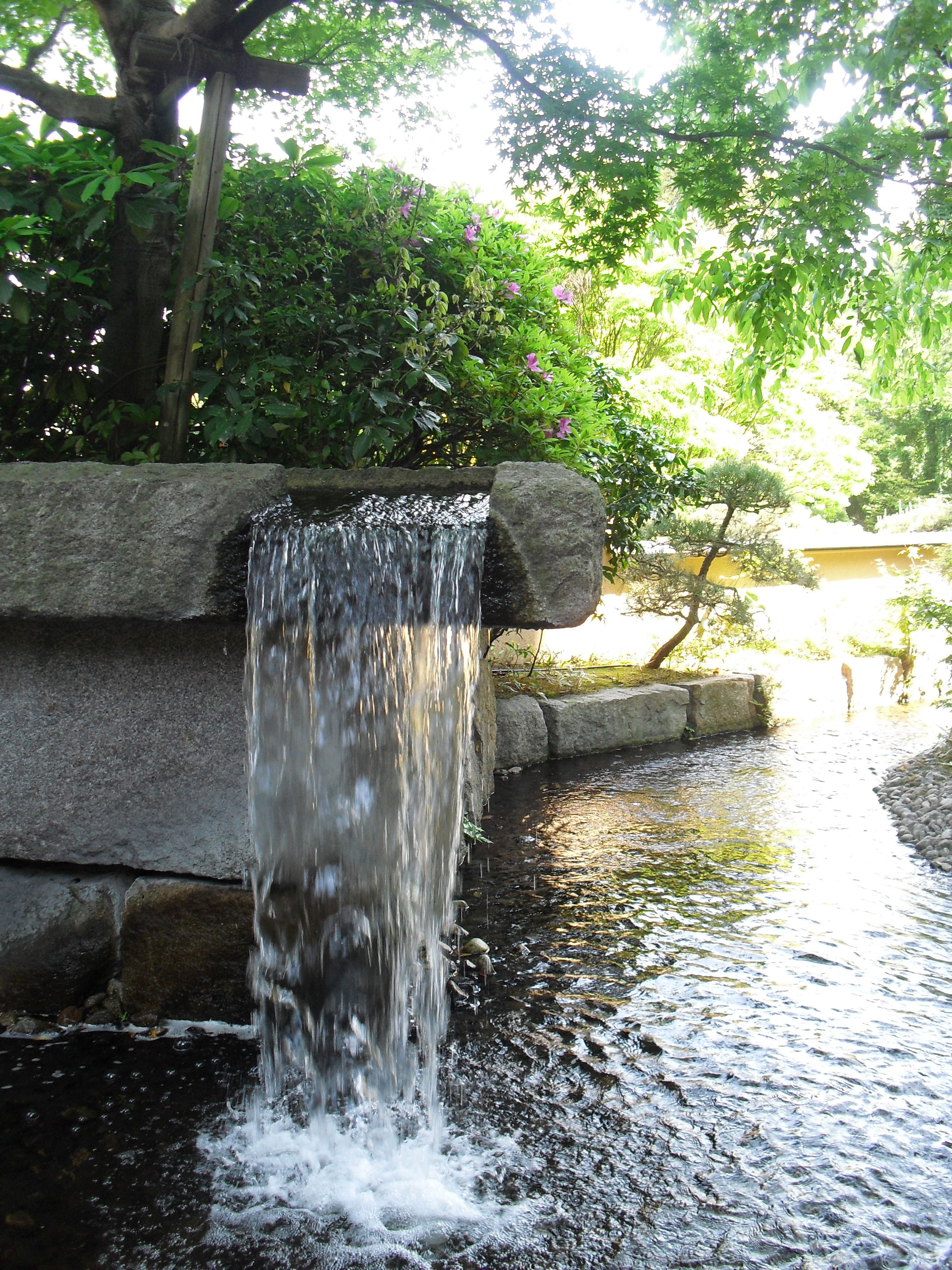 A waterfall cascading over a stone structure into a calm pool surrounded by lush greenery.