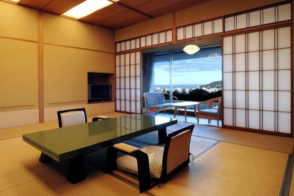 Una habitación tradicional japonesa con suelo de tatami, una mesa baja y vistas a un paisaje costero.