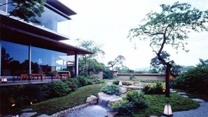 A modern house with a glass facade, a garden with a small waterfall, and outdoor seating. - Seizan Yamato (Ito)