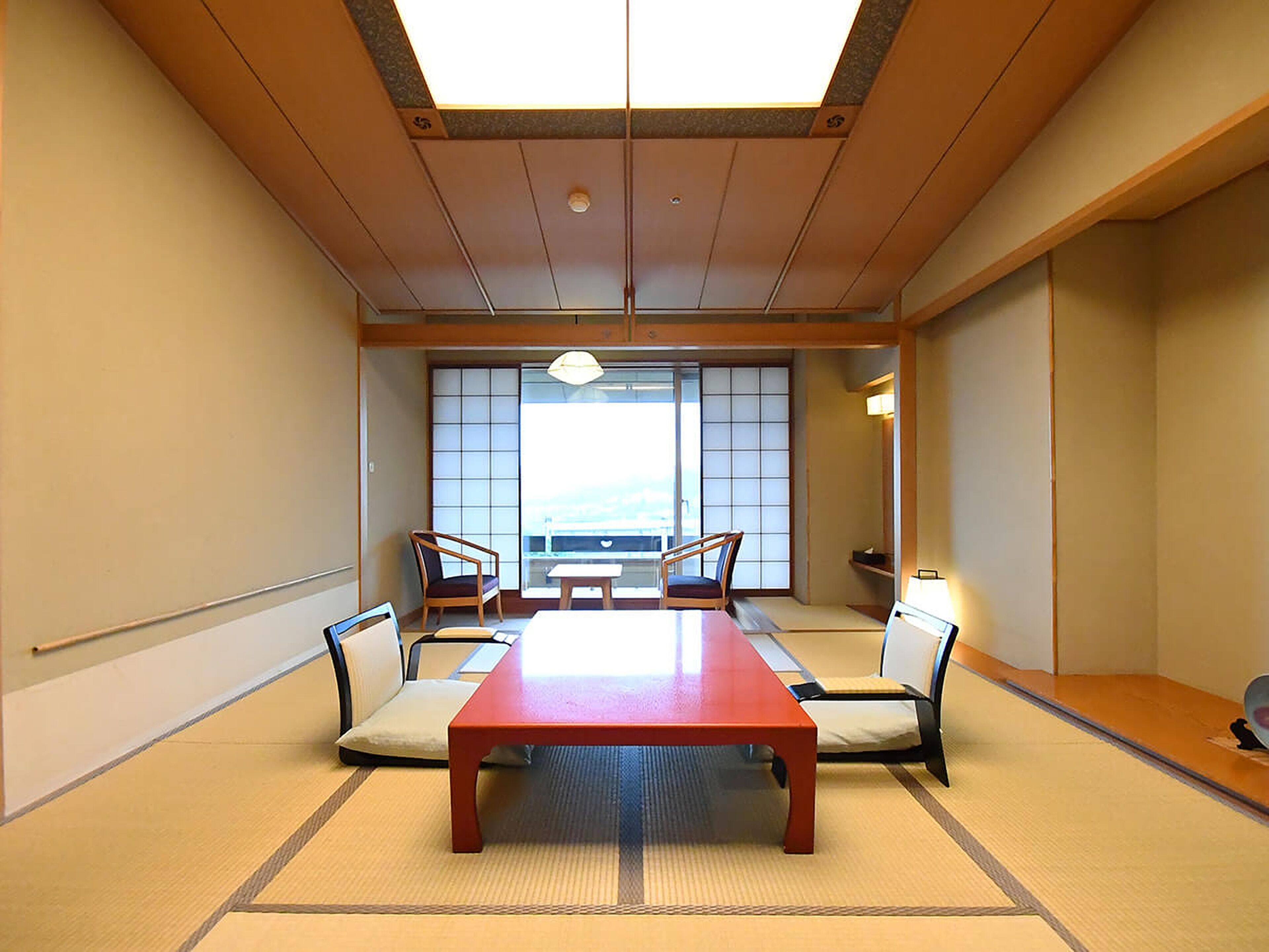 Ein Konferenzraum mit einem langen Tisch, vier Stühlen, Tatami-Matten, Schiebetüren und Ausblick durch die Fenster.