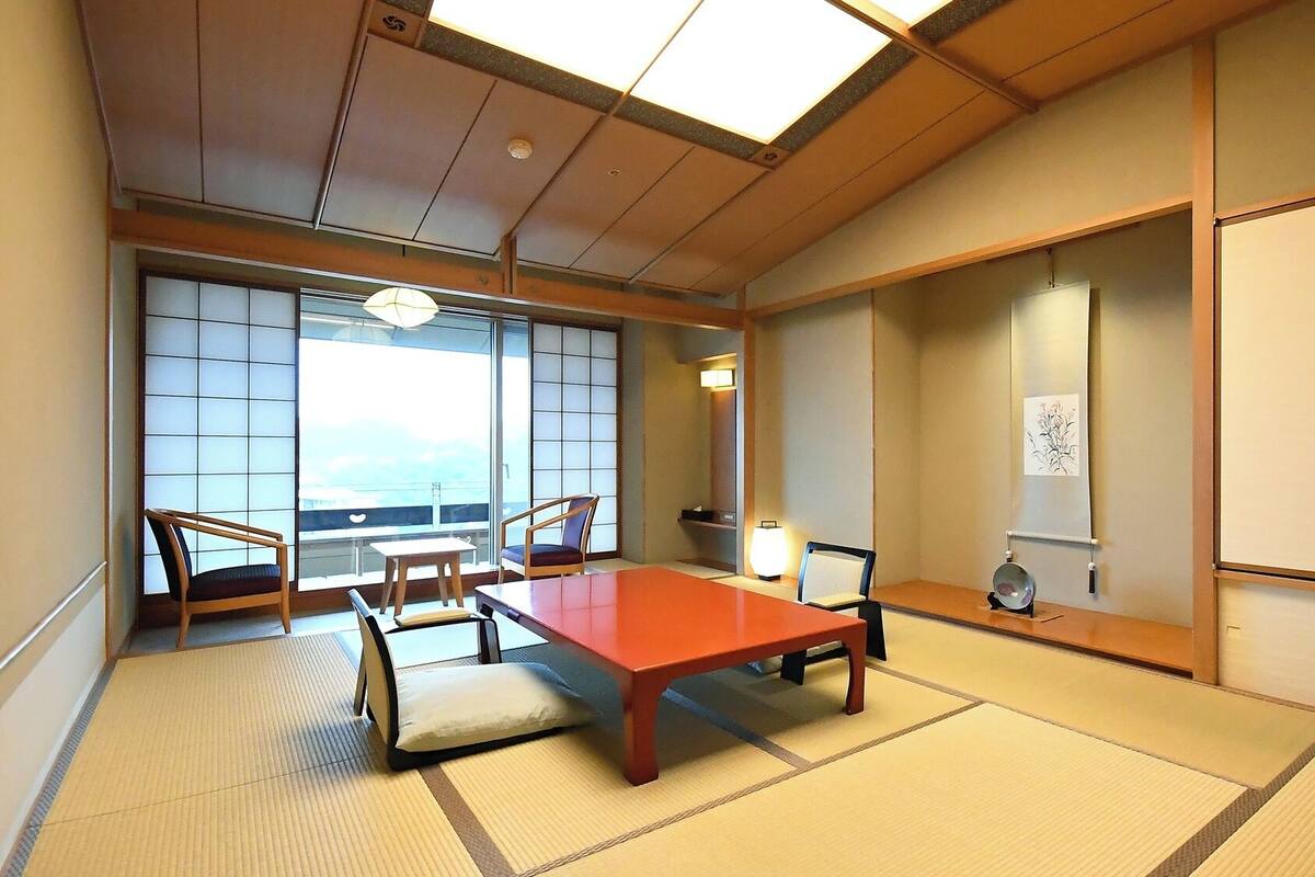 A traditional Japanese room with tatami flooring, a low table, chairs, a sliding door, and a view of the sea.