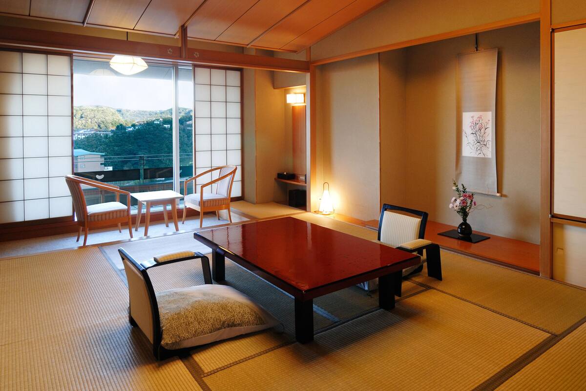 A traditional Japanese room with tatami flooring, a low table, and a view of a mountainous landscape.