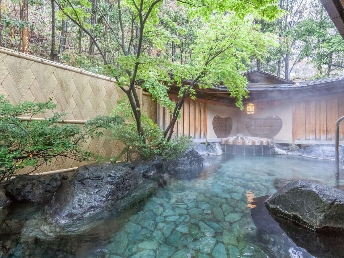 Un onsen japonés tradicional con una fuente termal cristalina rodeada de rocas y bambú.