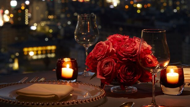 Cena romántica con vistas a la ciudad, velas y rosas rojas.
