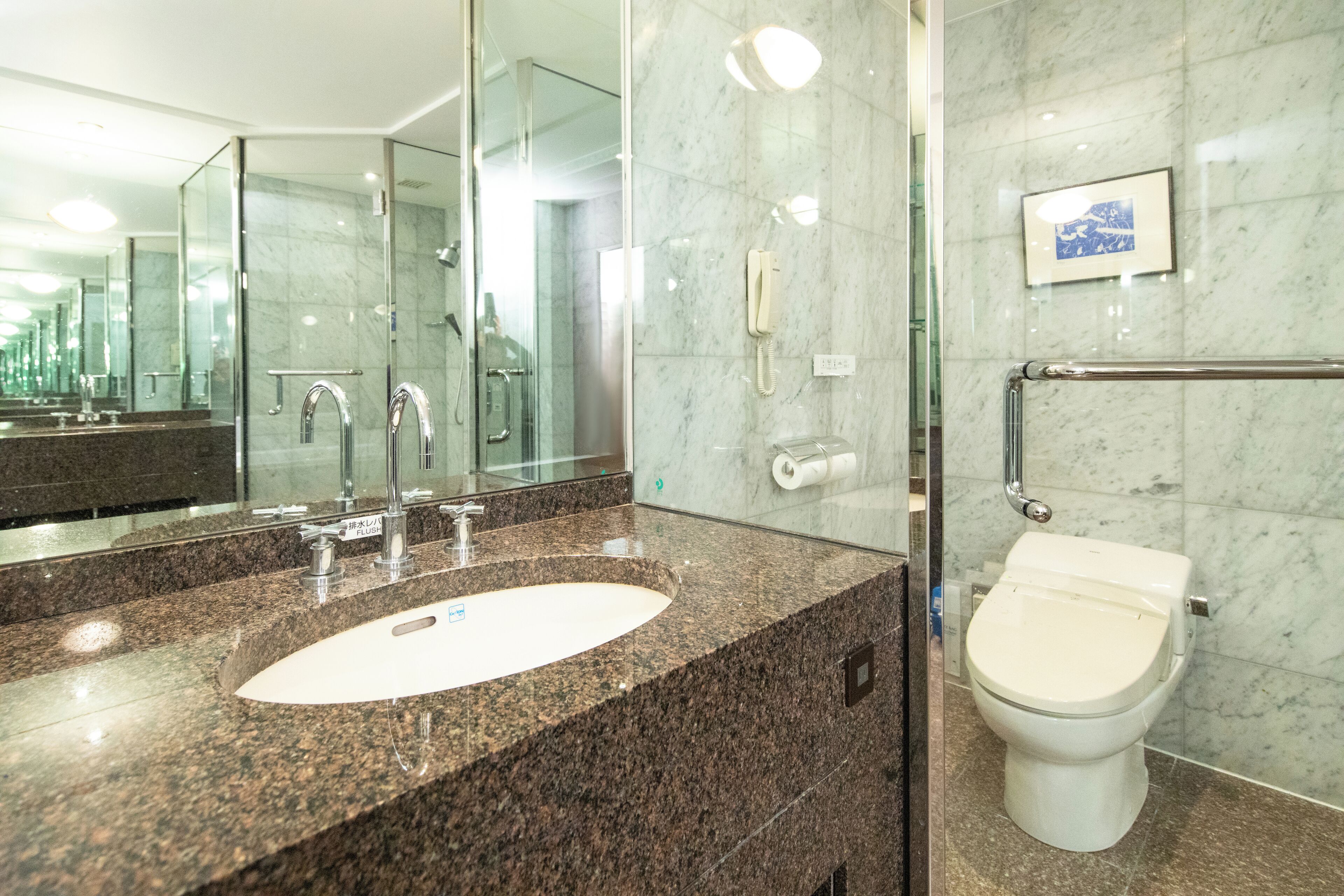 Une salle de bain moderne avec un lavabo sur un plan de travail en granit, une douche en verre, des toilettes et un mur en marbre.