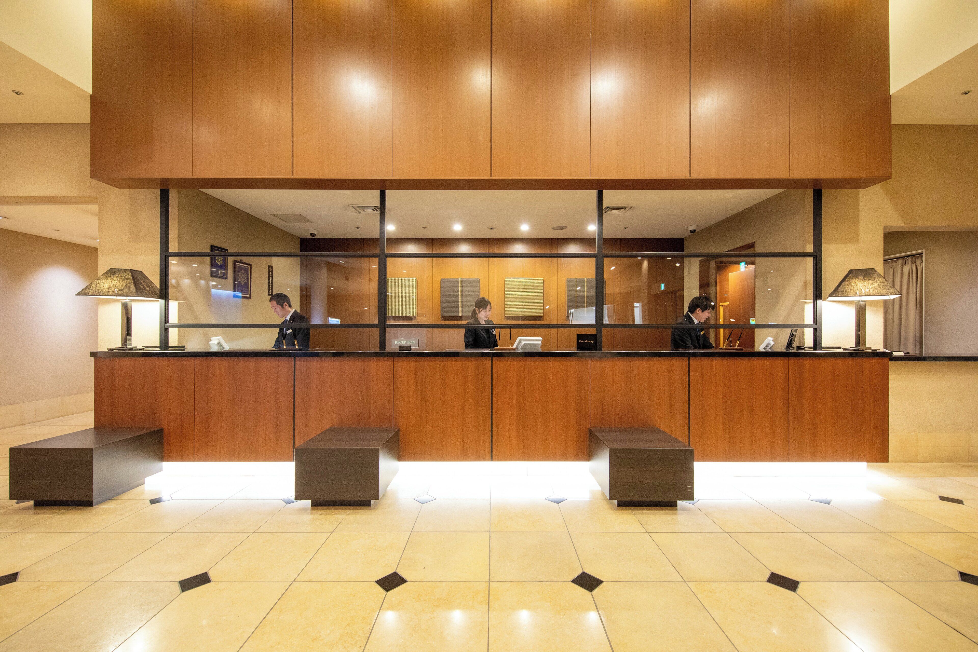 A reception desk with a wooden finish, a glass partition, and a tiled floor.