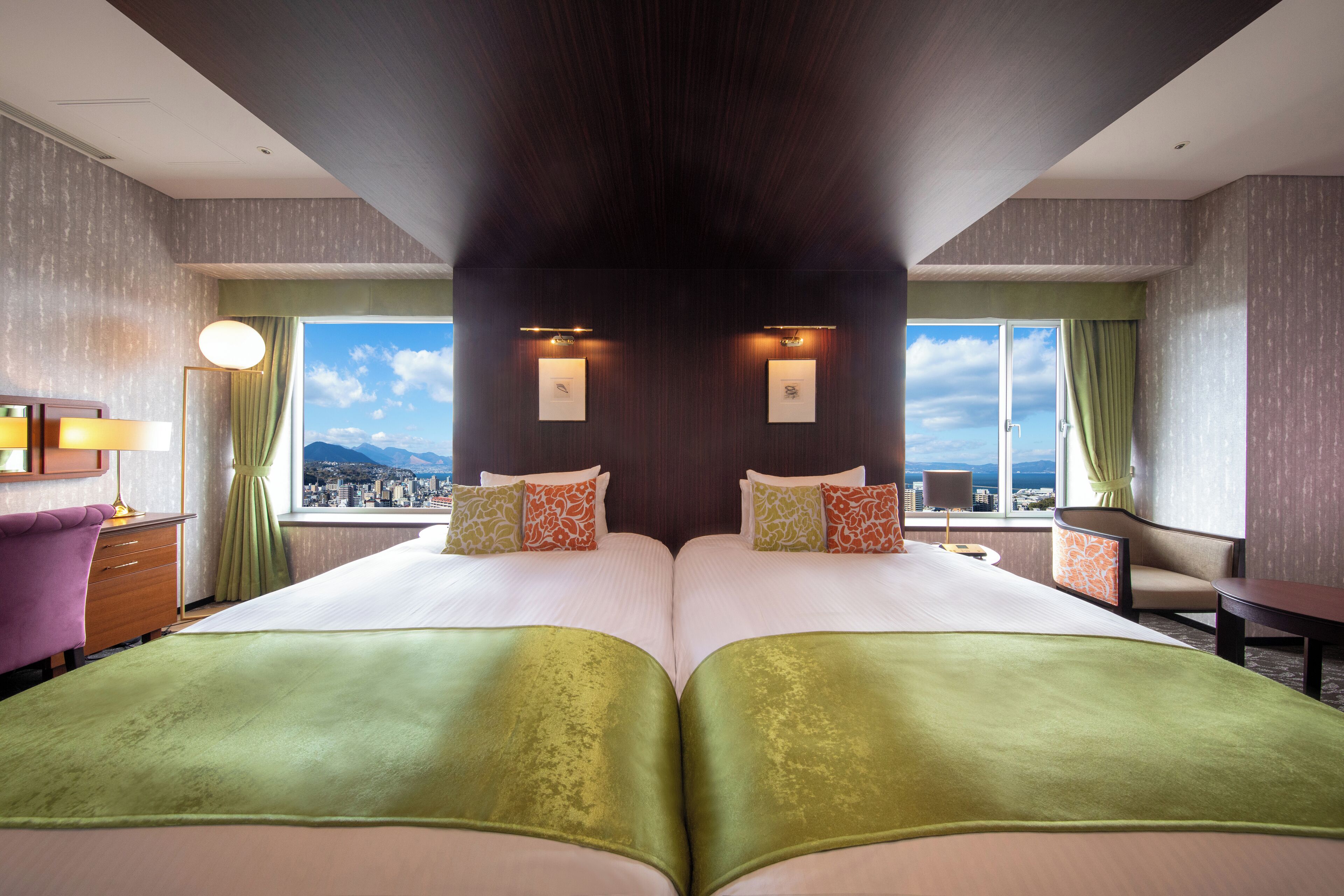 A hotel room with a large bed, two bedside tables, a chair, a desk, and a view of the city.