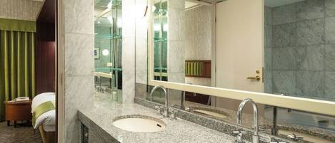 A hotel bathroom with two sinks, a large mirror, and a shower area.