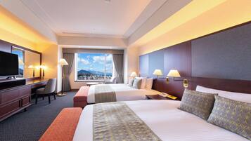 A hotel room with two beds, a desk, a TV, and a city view.