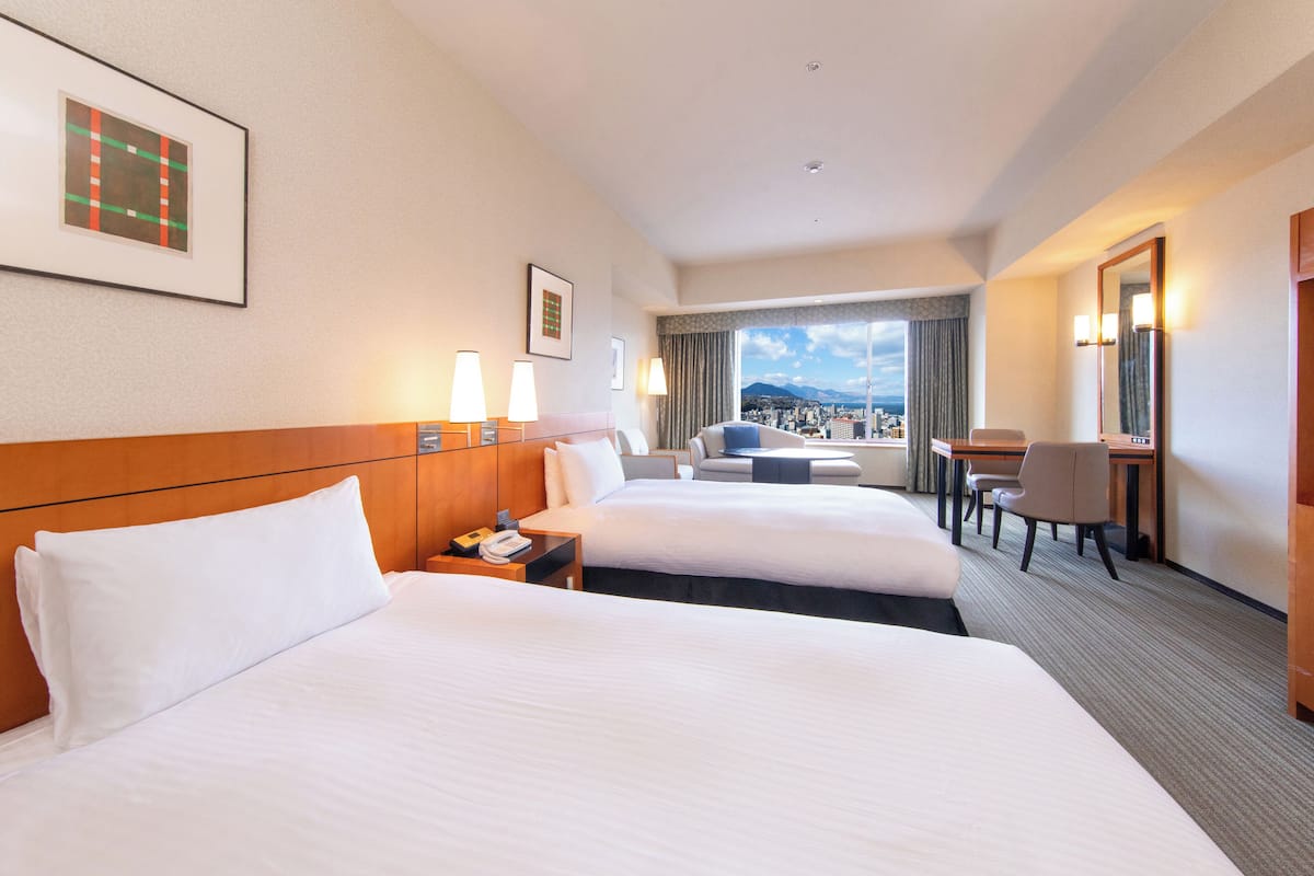 Habitació d'hotel amb dos llits, un escriptori, una cadira i vista a la ciutat.