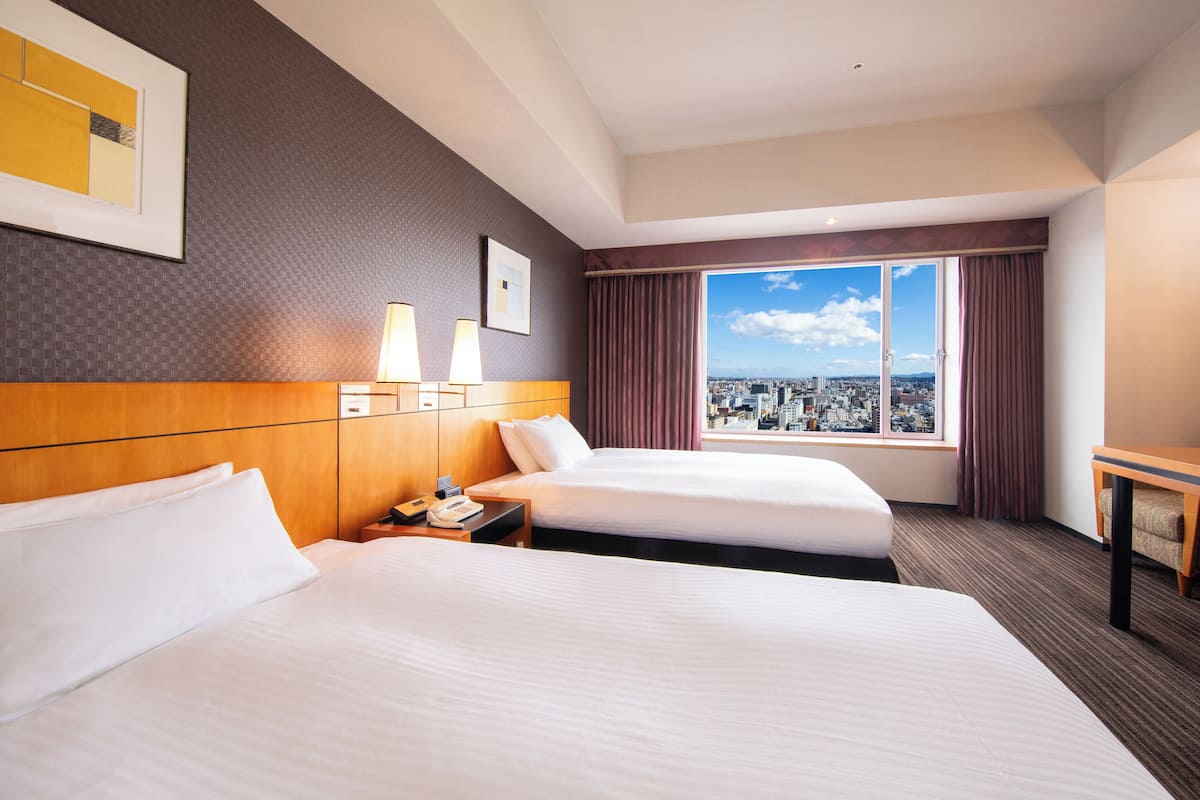 Habitació d'hotel amb dos llits, vista a la ciutat, escriptori i finestra amb cortines.