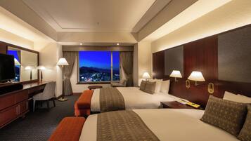 A hotel room with two beds, a desk, a chair, a TV, and a view of the city at night.