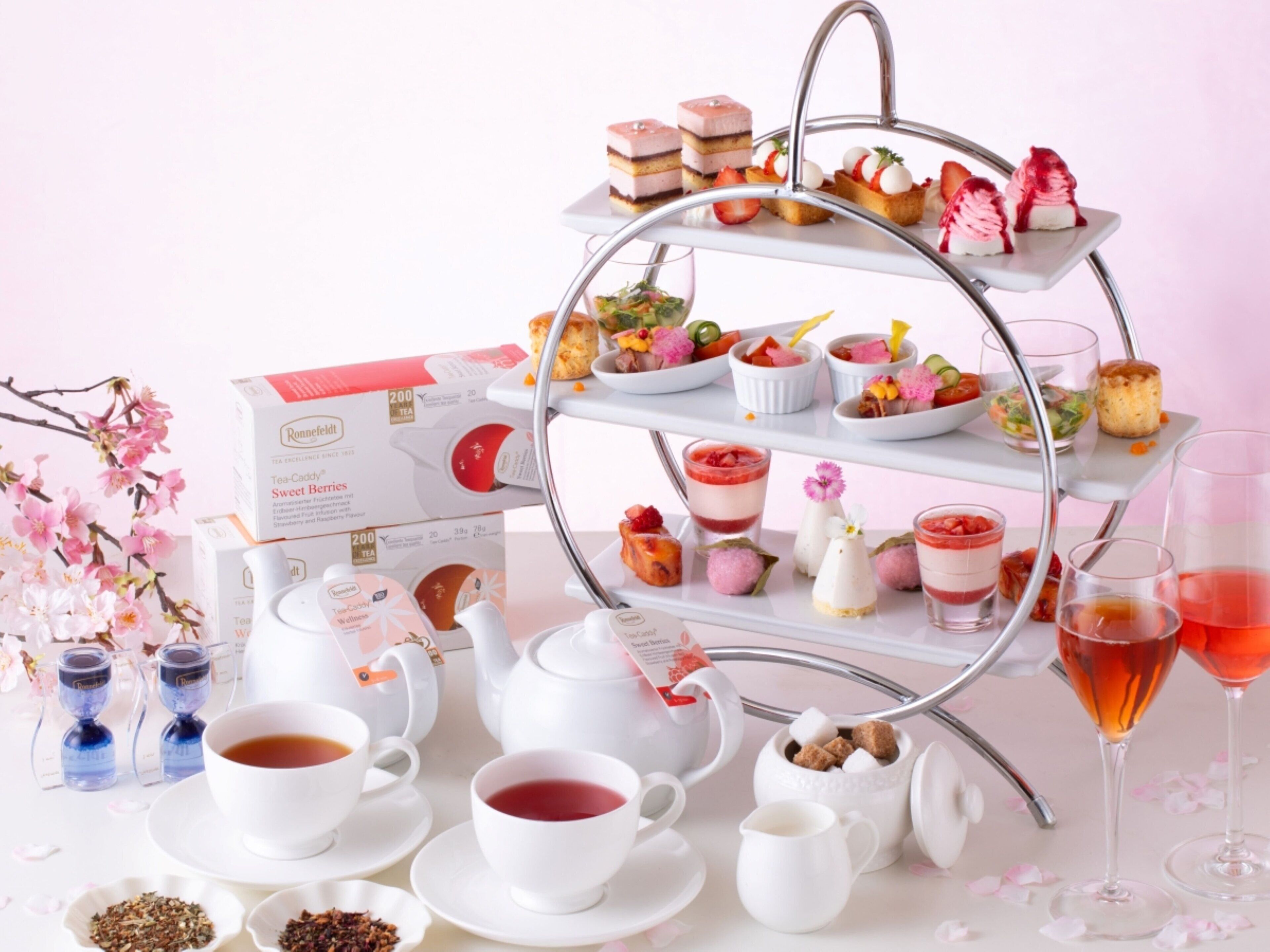 A tea service setup with a tiered stand holding various desserts, a tea set, and a glass of red beverage.