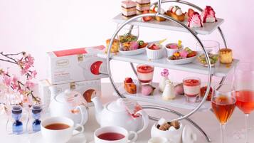 A tea service setup with a tiered stand holding various desserts, a tea set, and a glass of red beverage.