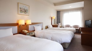 Una habitación de hotel con tres camas grandes, un escritorio con televisor y una ventana con cortinas.
