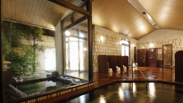 Un onsen japonés tradicional con interior de madera, manantial termal de piedra y vistas a un bosque de bambú a través de un amplio ventanal.