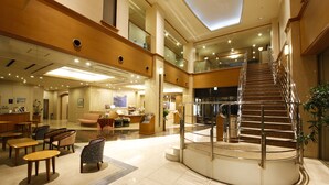 Un hall amplio con una escalera central, zonas de estar y un mostrador de recepción.