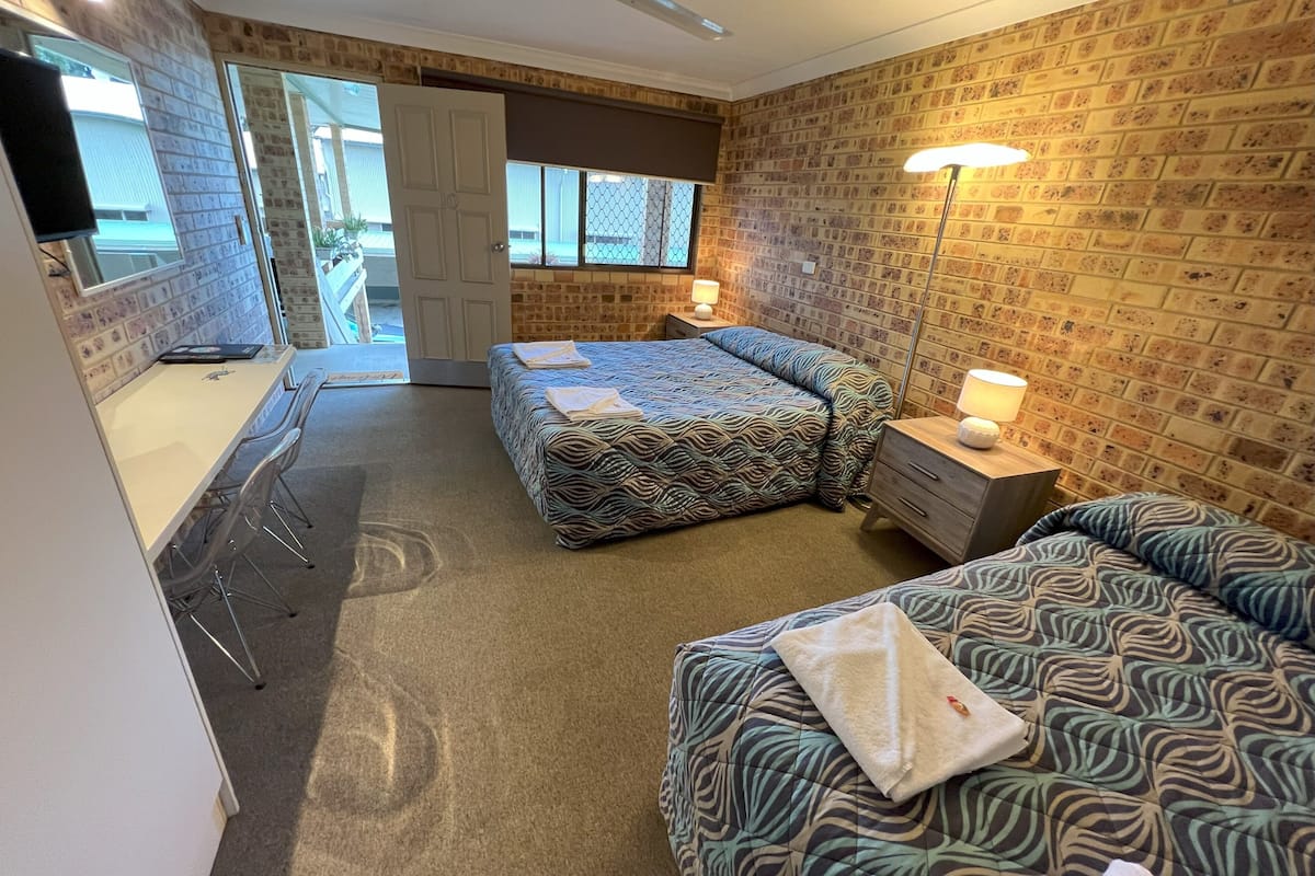 A hotel room with two beds, a desk, and a chair. There is a door leading to a balcony.