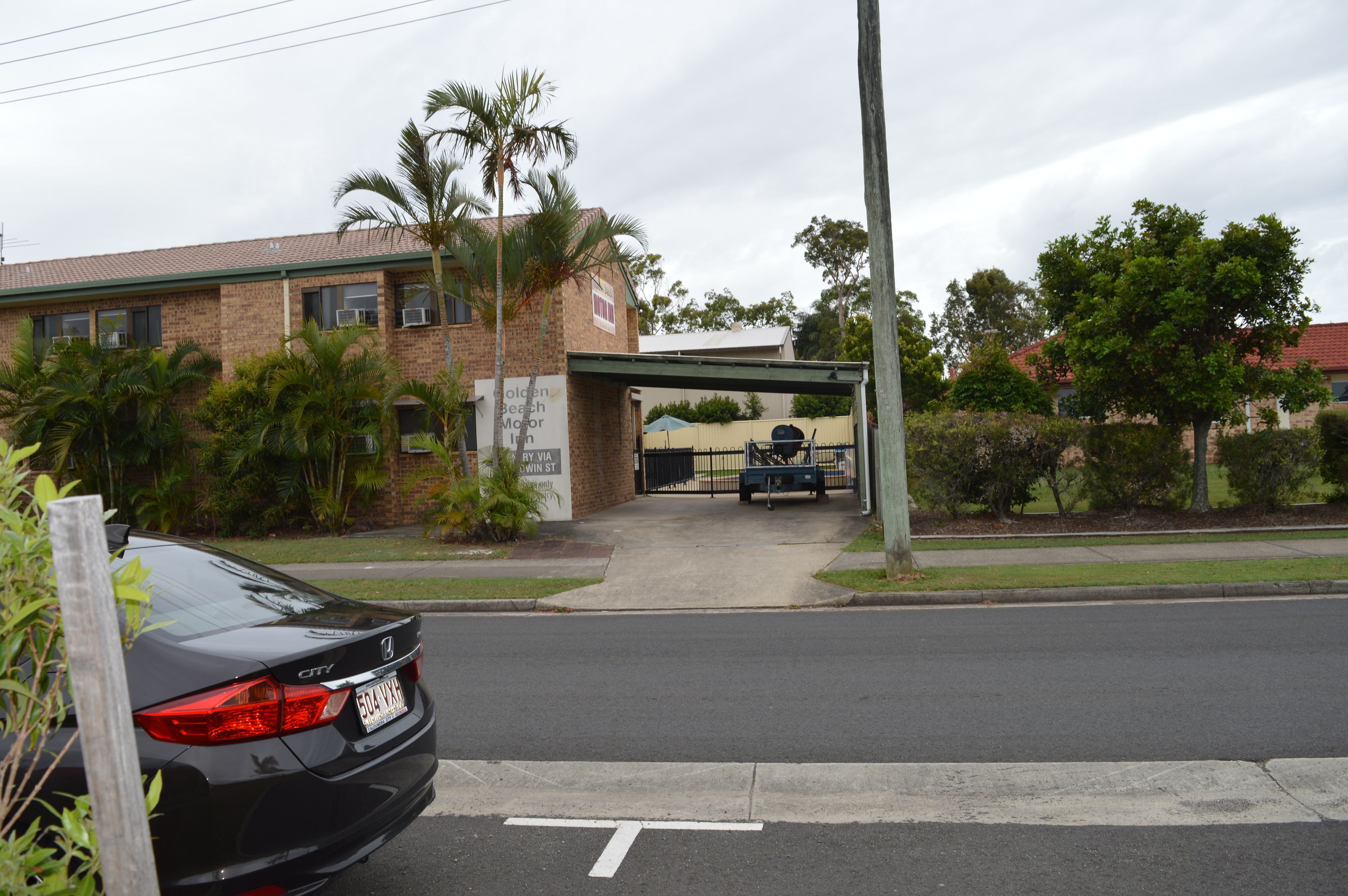 A black car parked on the street, a building with a sign for the Golden Beach Motor Inn, and a covered walkway leading to the entrance.