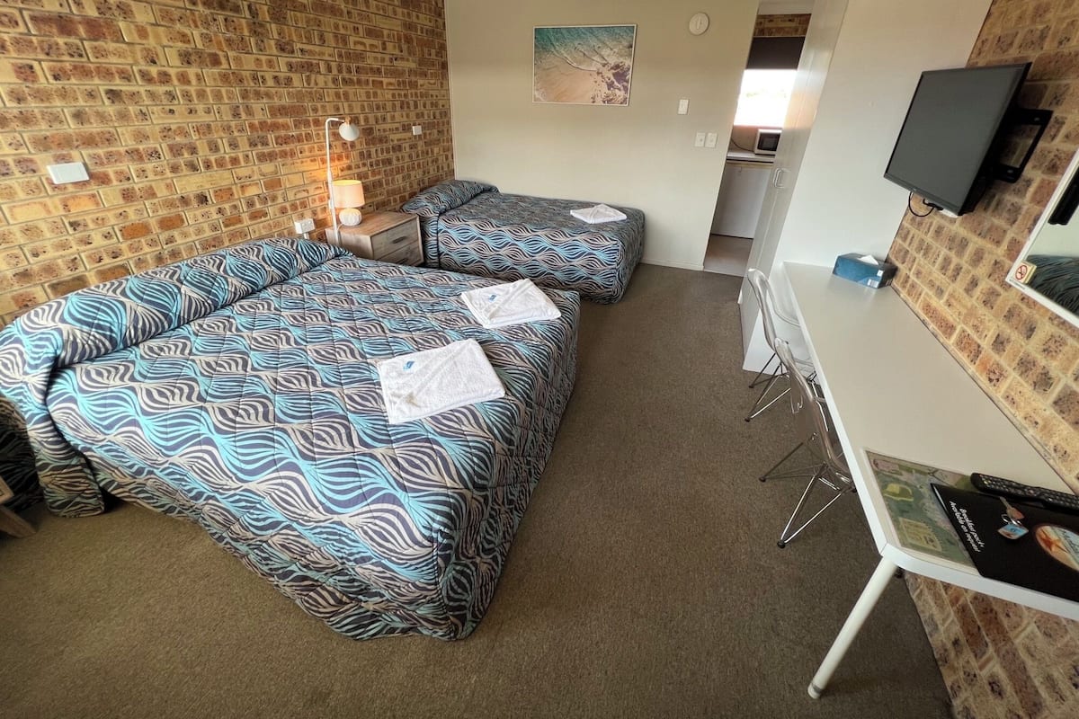 A hotel room with two beds, a desk, a television, and a brick-patterned wall.