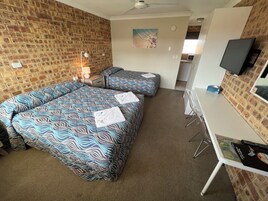 Habitación de hotel con dos camas, un escritorio, un televisor y una pared con diseño de ladrillo.