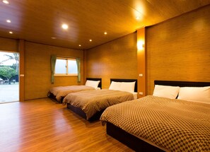Une chambre d’hôtel avec trois lits, un plancher en bois et une grande fenêtre avec des rideaux.