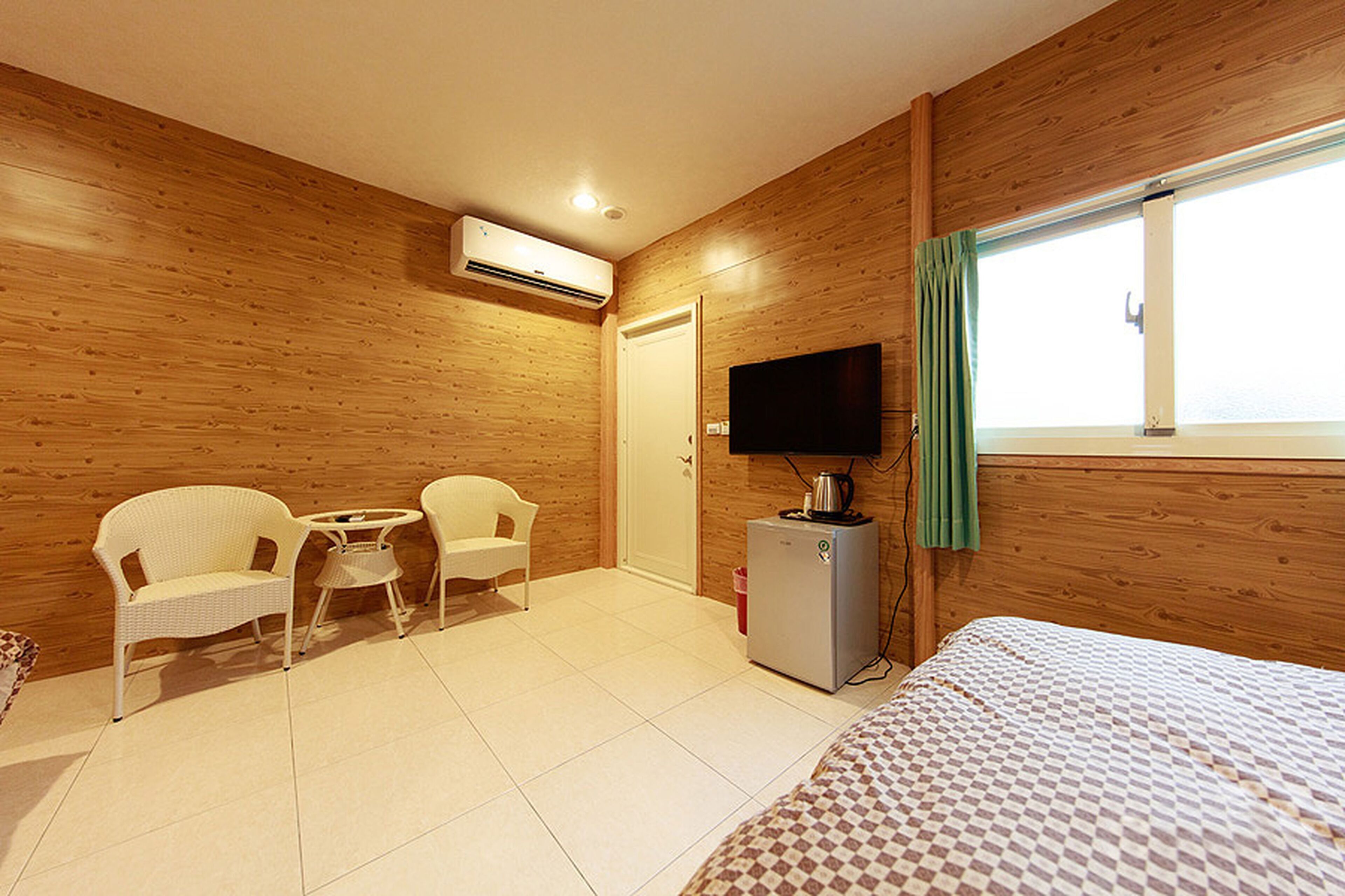Una habitación con paredes de madera, una cama, un televisor, una mesita pequeña, dos sillas y un equipo de aire acondicionado.