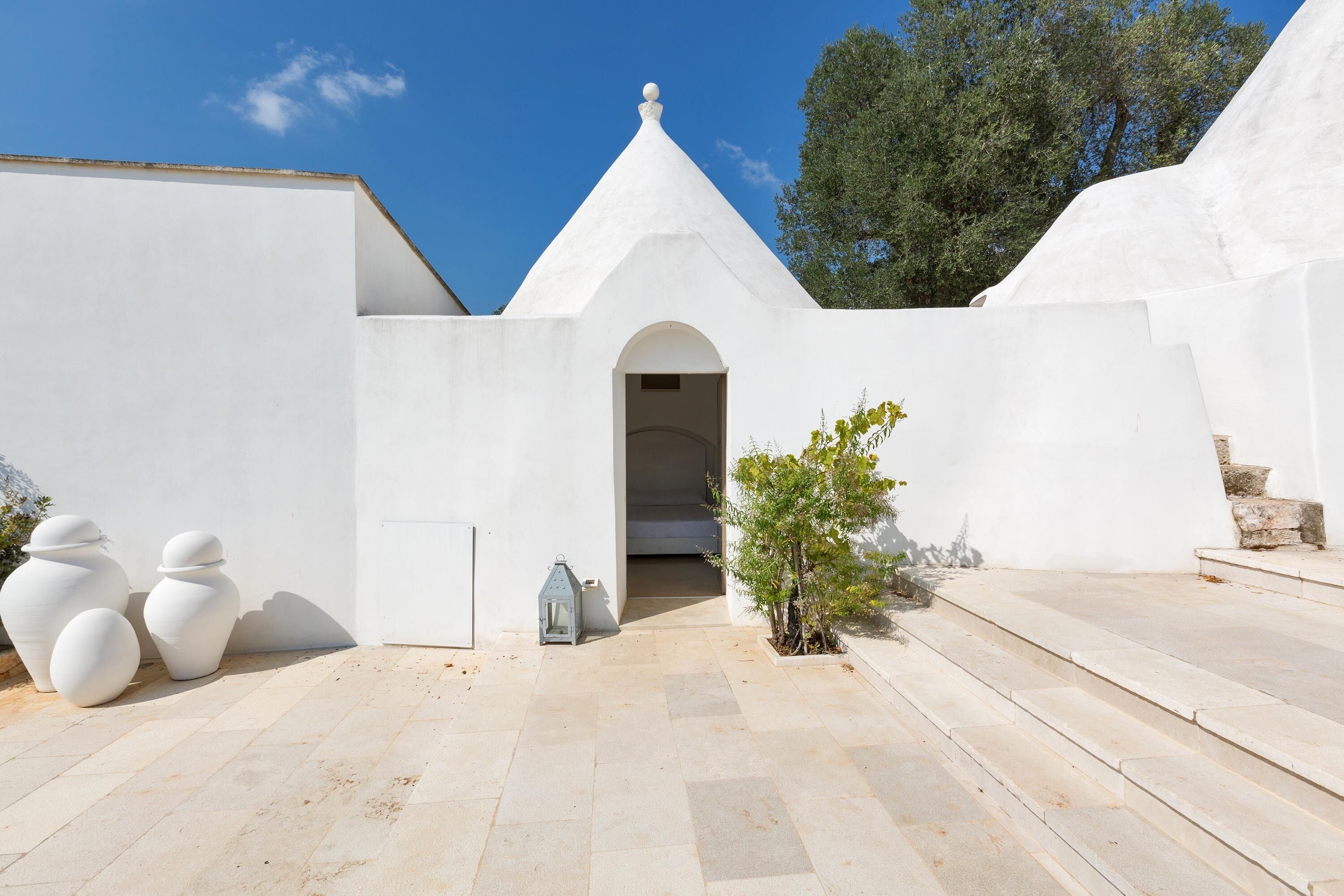 A white building with a conical roof, a small tree, and a lantern.