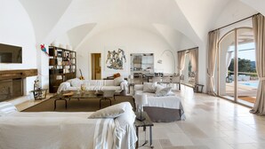 A spacious living room with a fireplace, a dining area, and a kitchen. There is a large window with curtains and a view of the outdoors. - Casa Murredda (Ostuni)