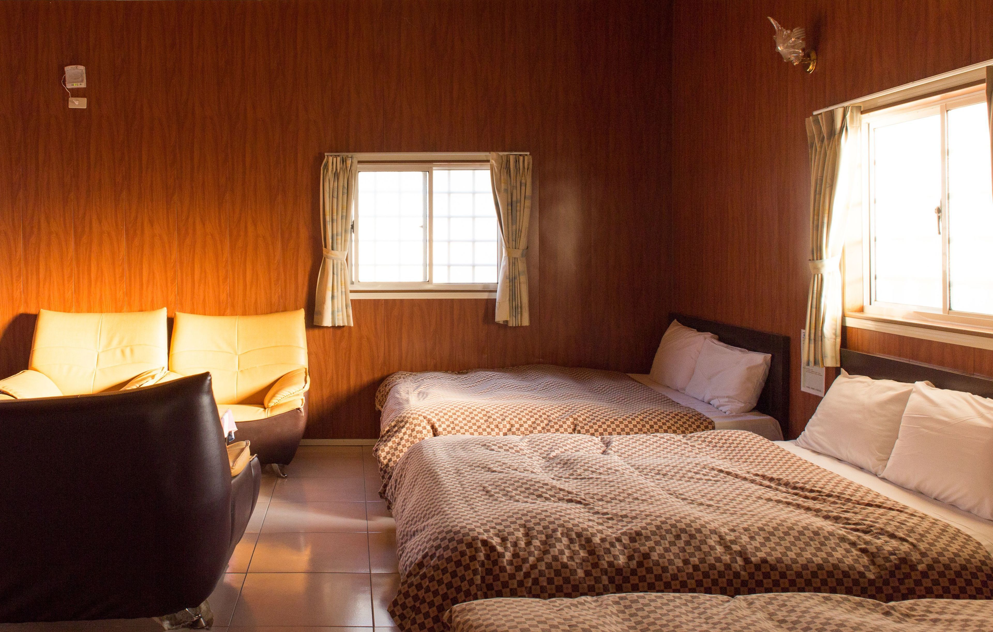 A room with two beds, a chair, and a window with curtains.