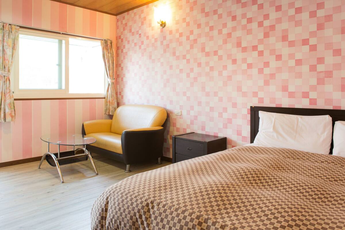 Una habitación con cama, una silla, una mesita y una mesita de noche.