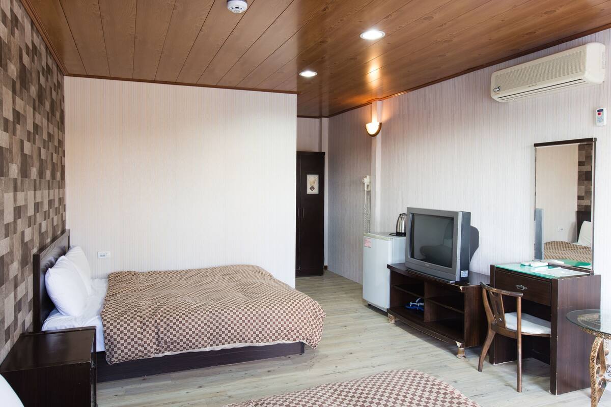 Un dormitorio con una cama, un escritorio con televisor, una silla y un equipo de aire acondicionado.