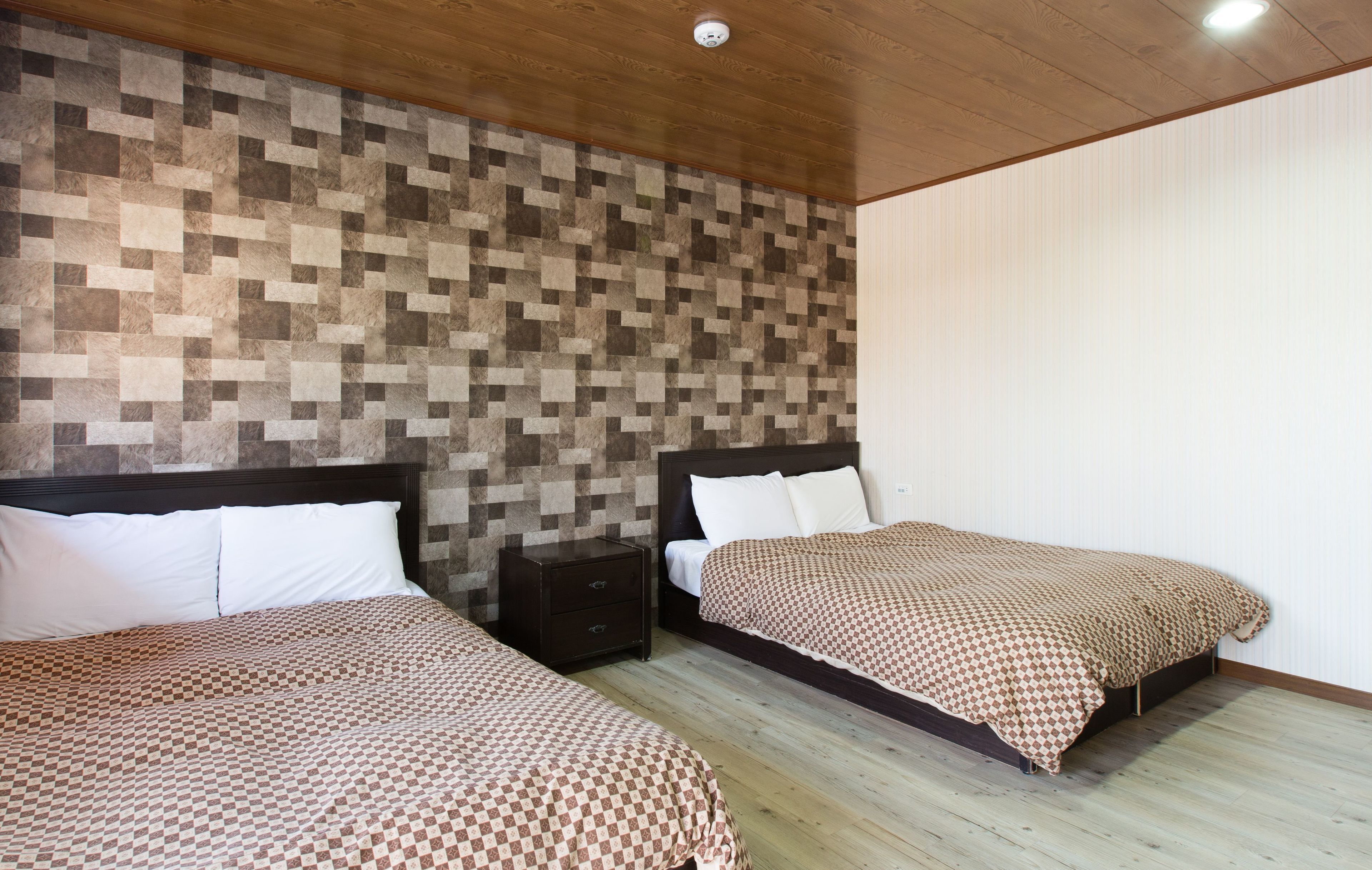 Une chambre avec deux lits, un plafond en bois et un mur orné d’un motif en mosaïque.