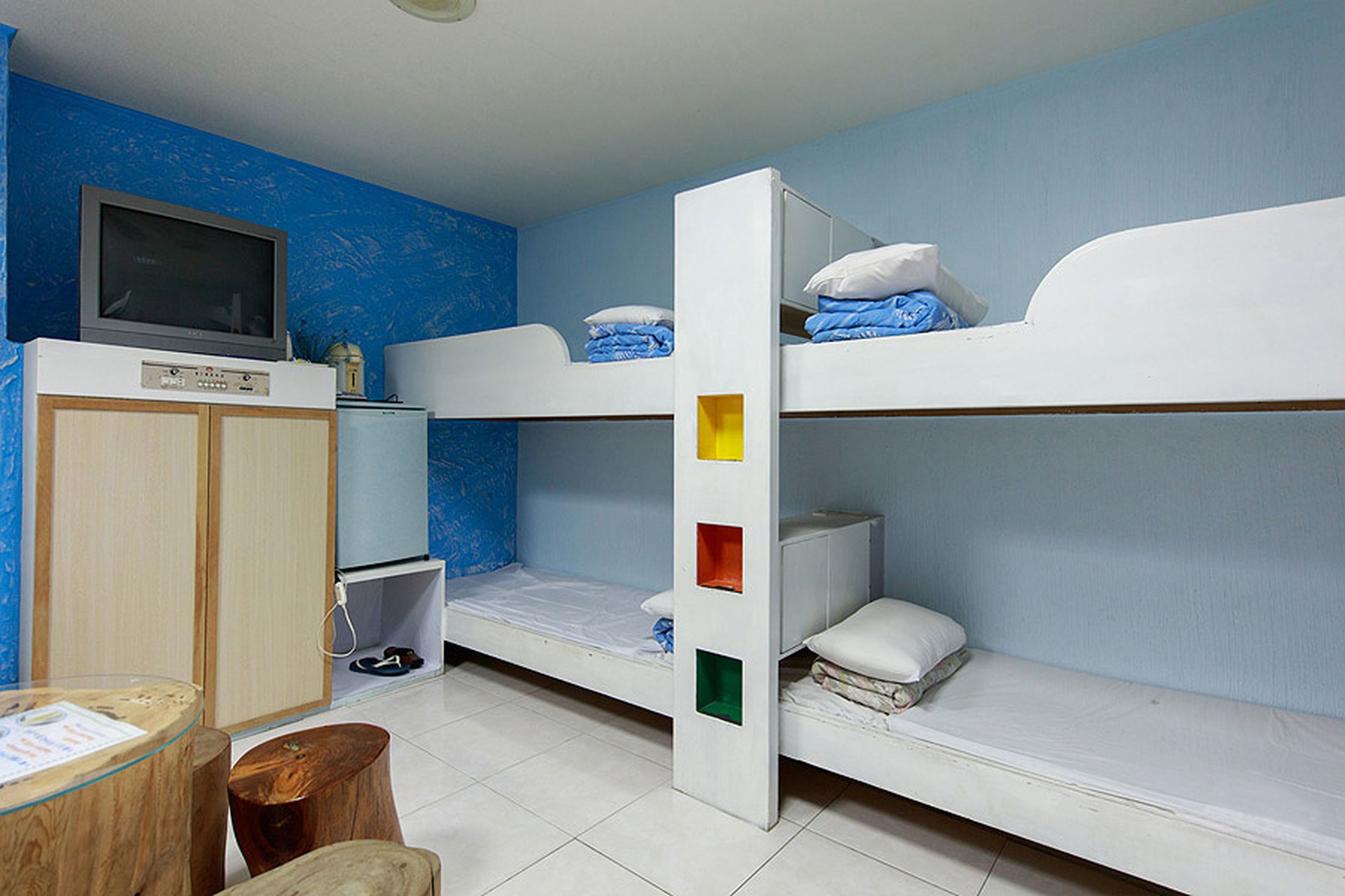 Une chambre avec un lit superposé, une télévision, une armoire en bois et une petite table.