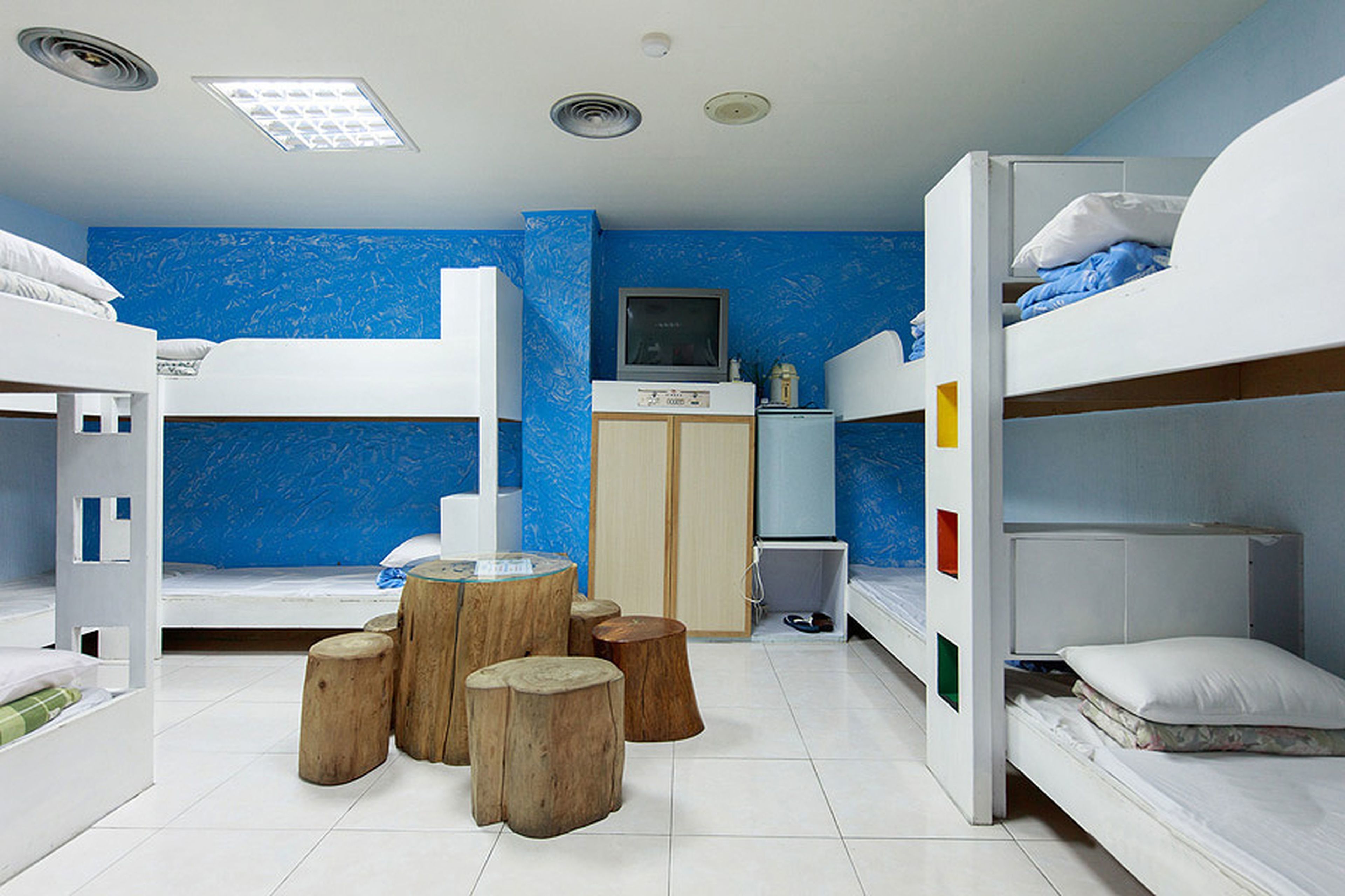 A room with bunk beds, a television, and wooden stools.