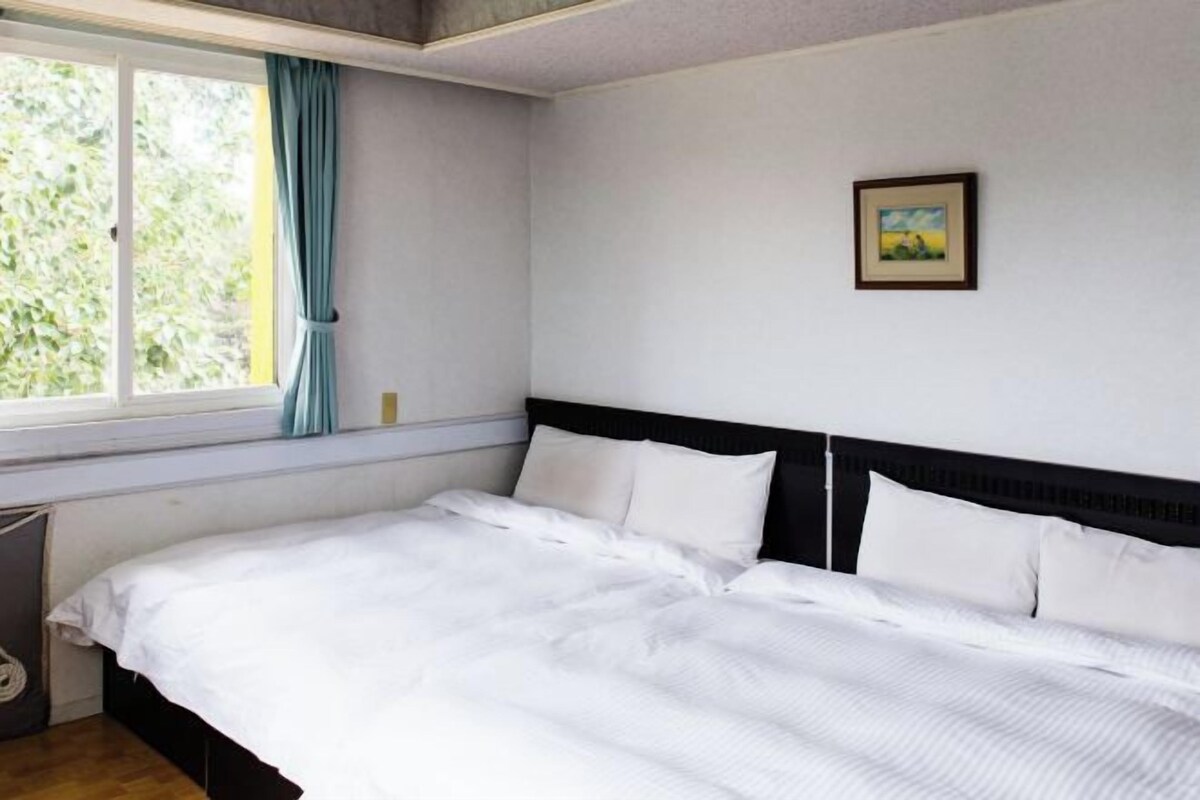 A bedroom with a bed, a window with curtains, and a framed picture on the wall.