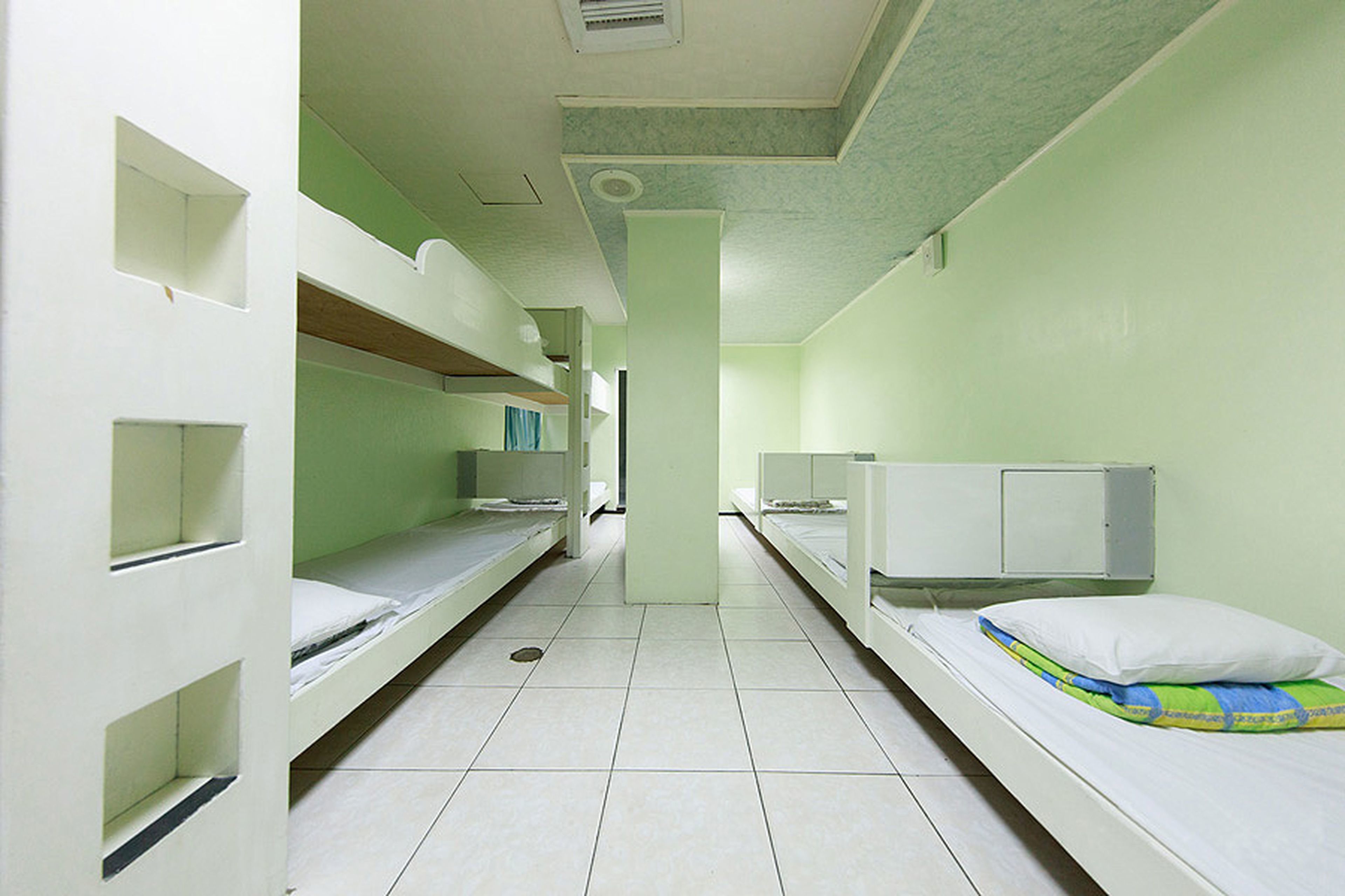 A dormitory room with bunk beds, a central pillar, and a tiled floor.